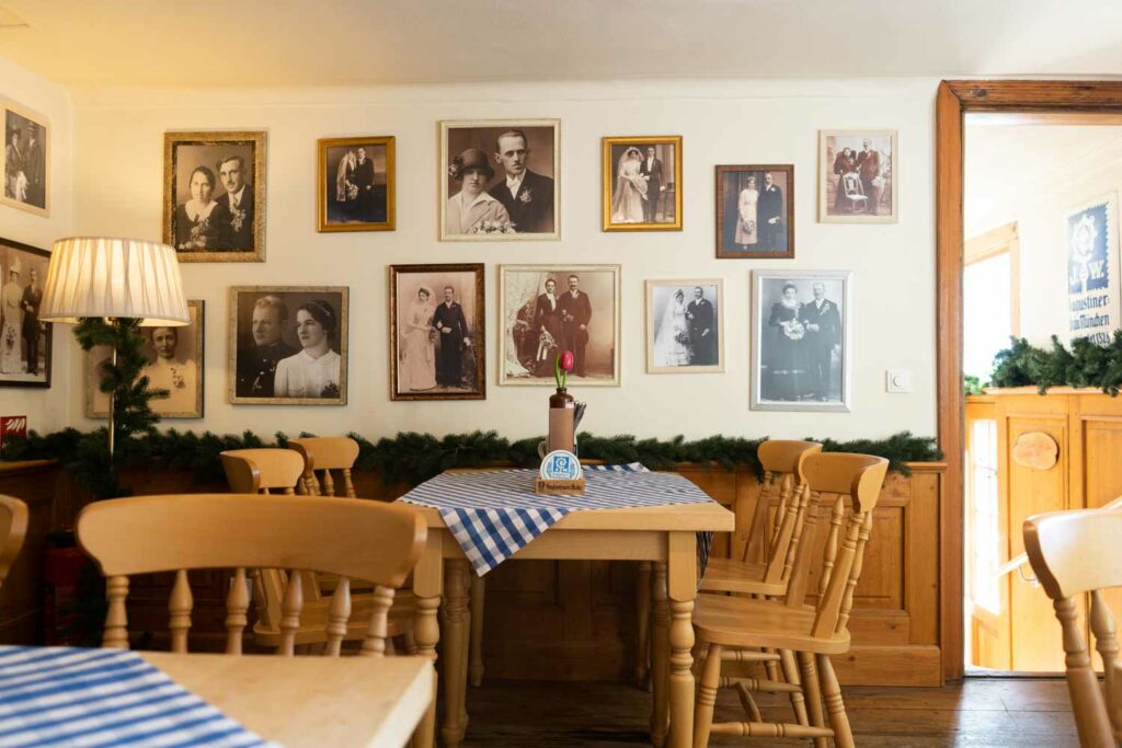 Traditionell eingerichteter Speiseraum mit hellen Holzstühlen, blau-weiß gedeckten Tischen und nostalgischen Bildern an der Wand.